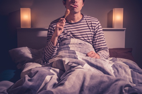 Young-man-is-sitting-in-bed-and-eating-chicken iStock