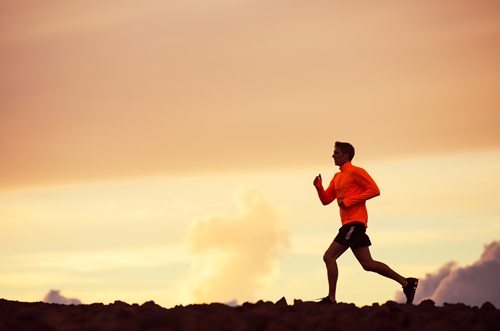 Male runner wearing bright clothing running into sunset