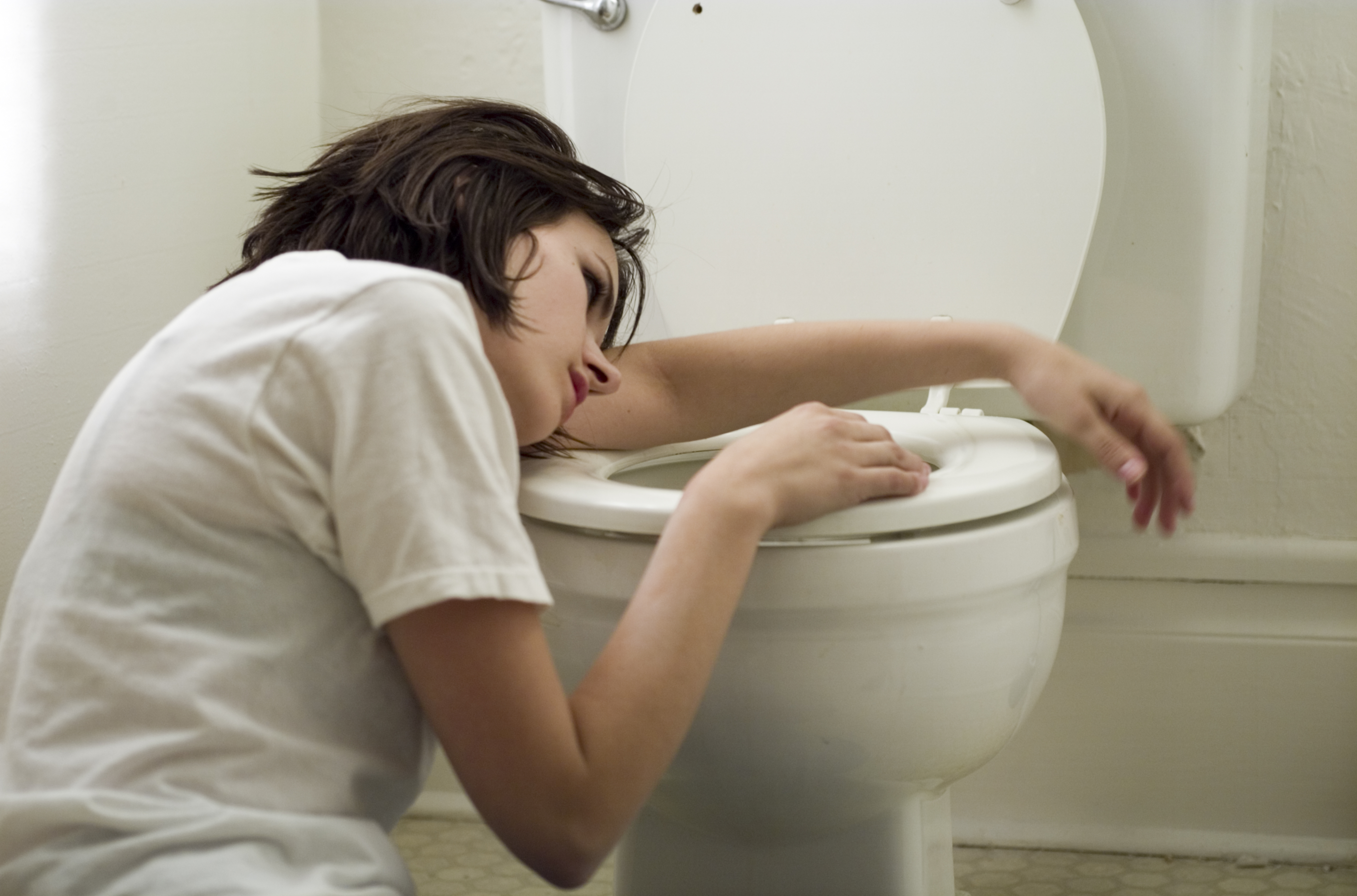 Sick young woman leaning on toilet bowl