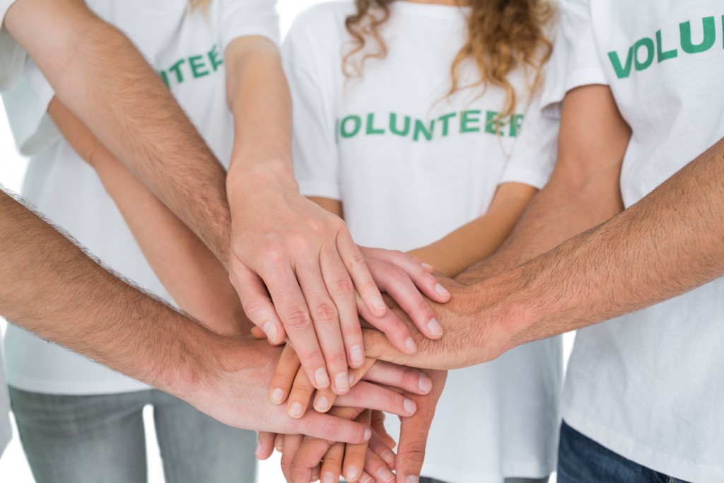 Close-up mid section of volunteers with hands together over white background
