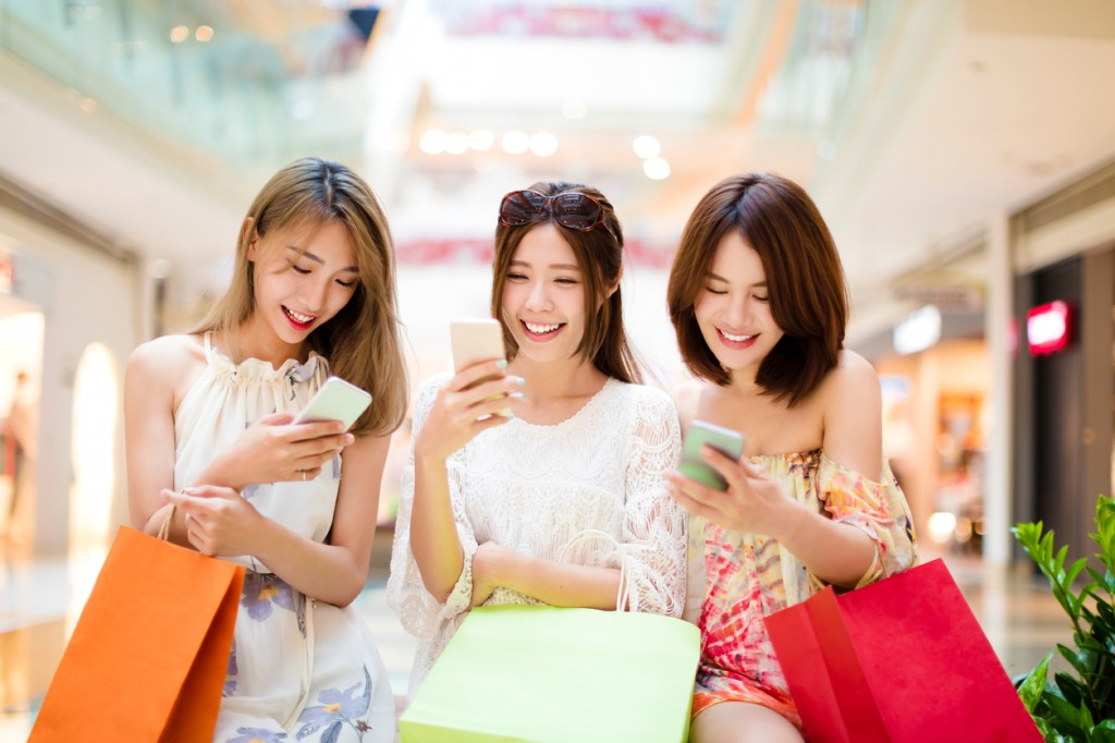 happy young woman watching smart phone in shopping mall