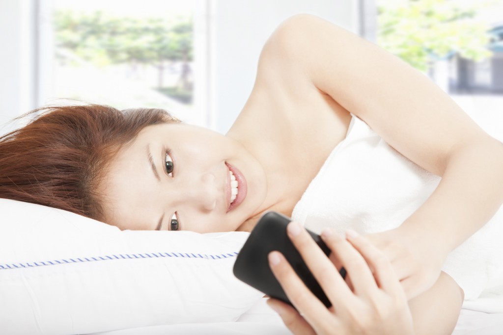 young woman looking smart phone on the bed