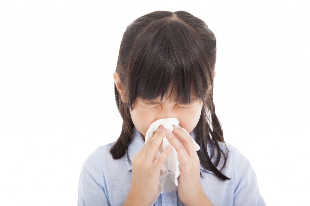 Young girl blowing her nose into a tissue