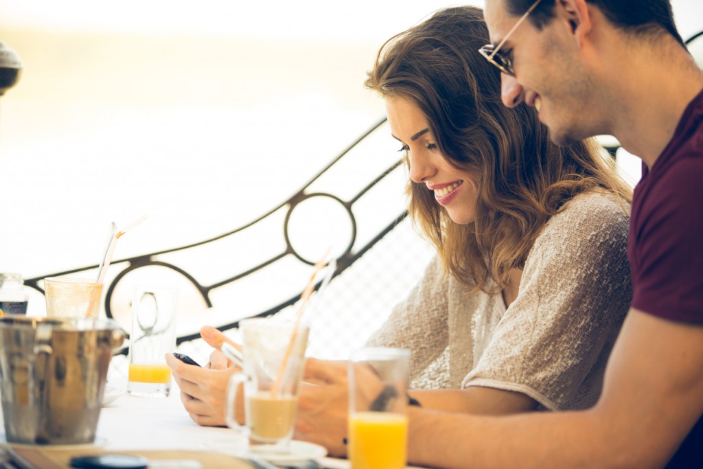 Couple reading and typing text messages on mobile in cafe