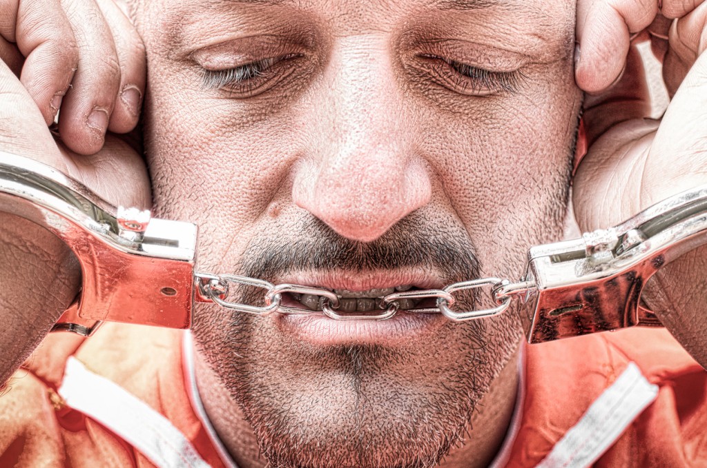 Sad depressed detained man with handcuffs in prison