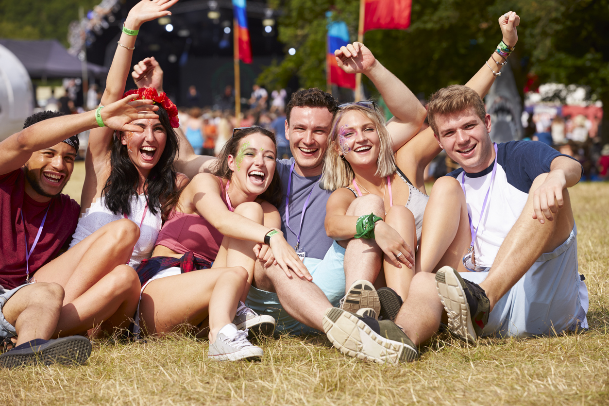 Friends sitting on the grass cheering at a music festival