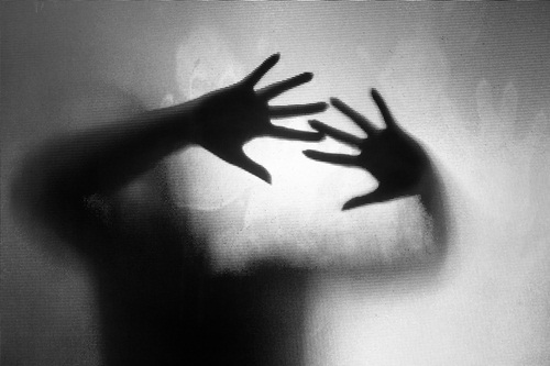 Spooky silhouette of woman with hands pressed against glass window