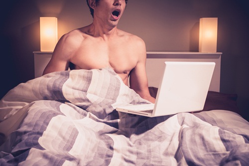 Young man in bed watching pornography on laptop