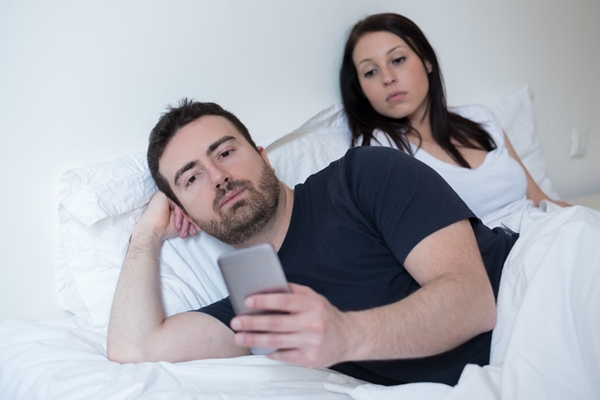 Man neglecting his girlfriend and using his mobile phone in bed