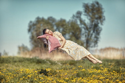 Girl hovers and sleeps on a pillow over a beautiful meadow.