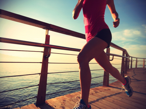 young fitness woman legs running on sunrise seaside trail